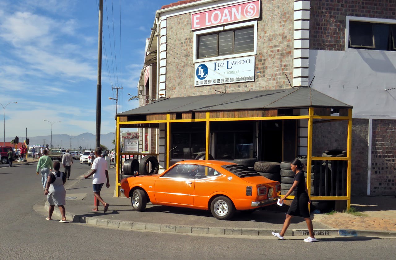 A vintage orange car parked outside a brick building with a tire shop, capturing urban street life.